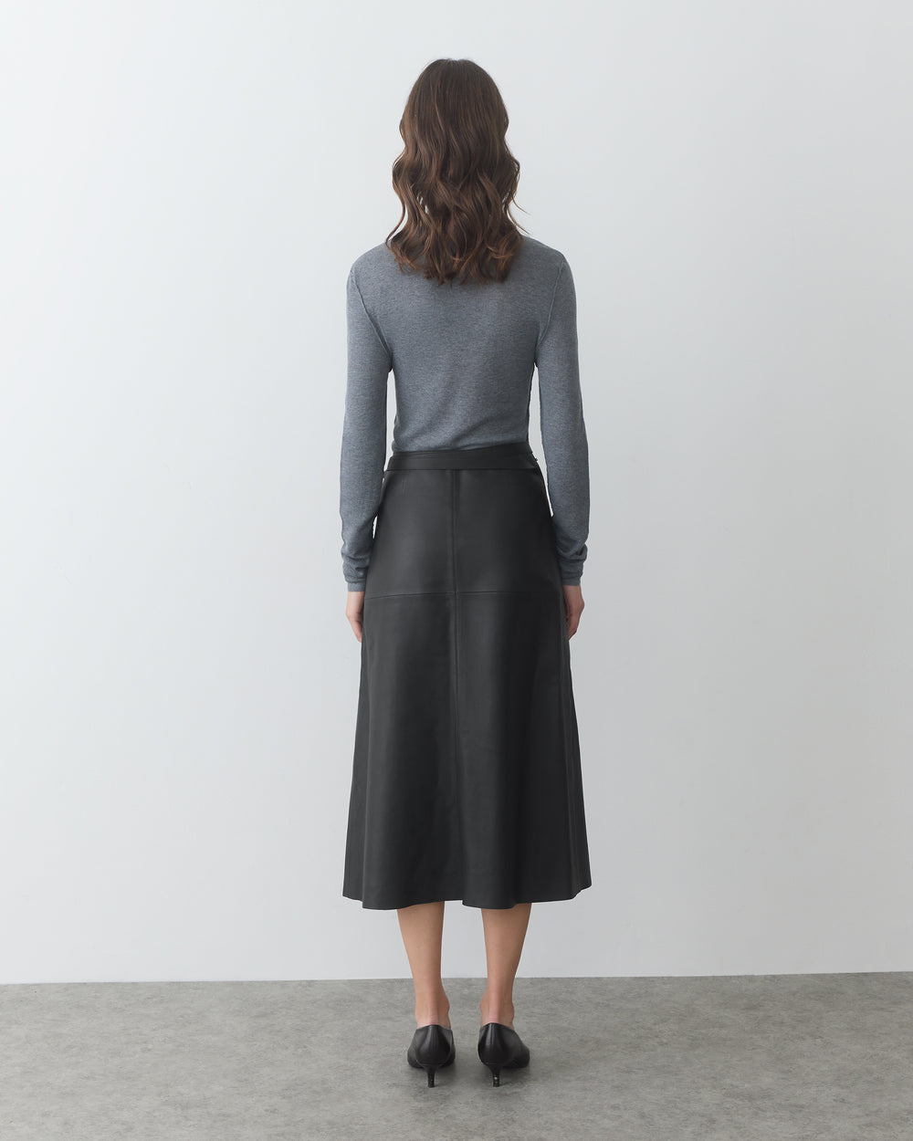 Person facing wall wearing long-sleeve shirt and long skirt.