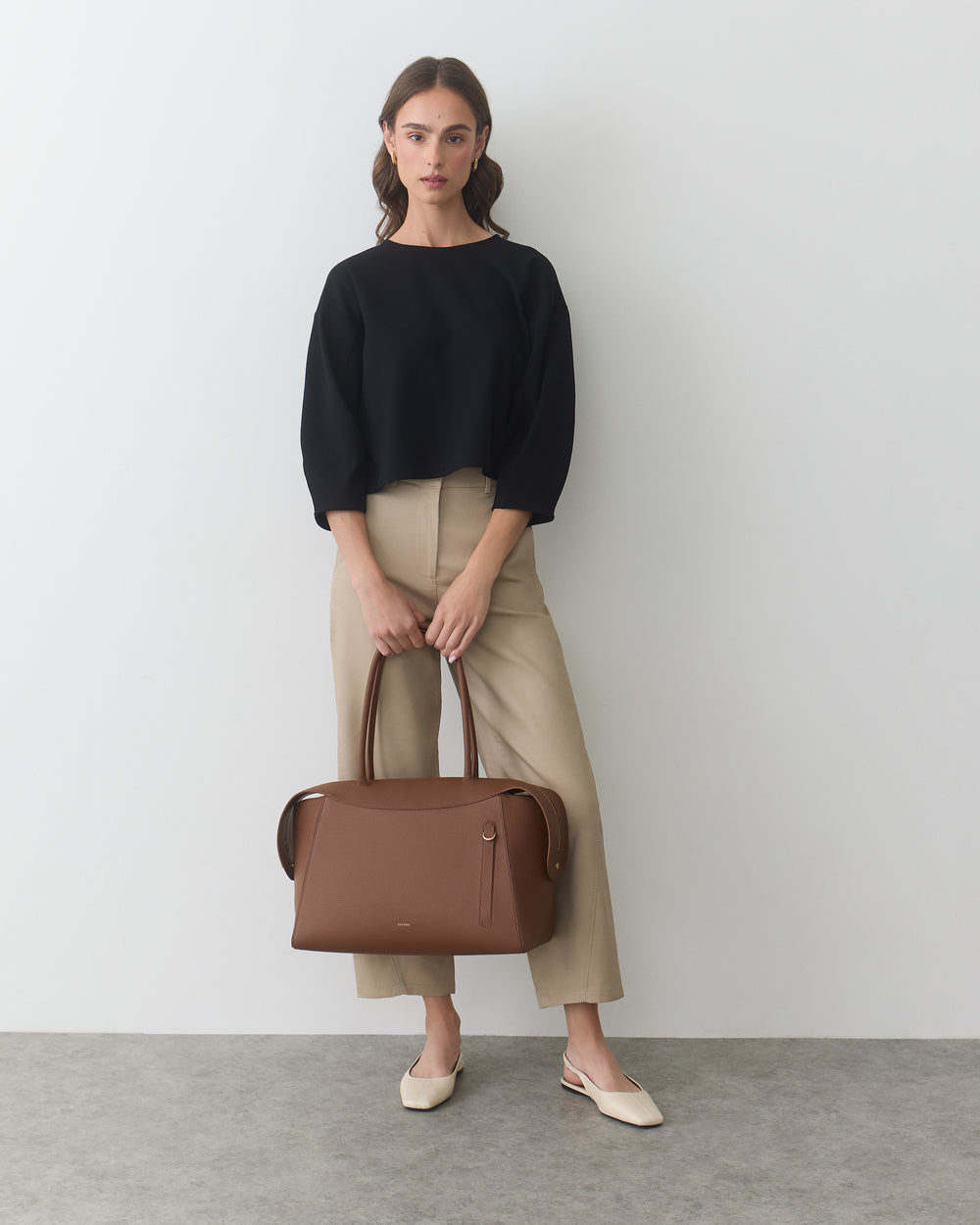 Person standing with a travel bag wearing a long-sleeve top and pants.