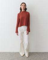 Person in long-sleeve top and wide-leg pants standing indoors.