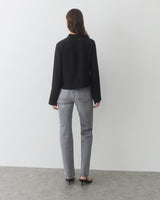 Person wearing long-sleeve top, jeans, and heels, standing in a plain indoor setting.