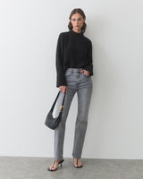 Person in long-sleeve top and jeans holding shoulder bag, wearing heeled sandals.