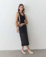 Person in dress holding a handbag standing against a wall