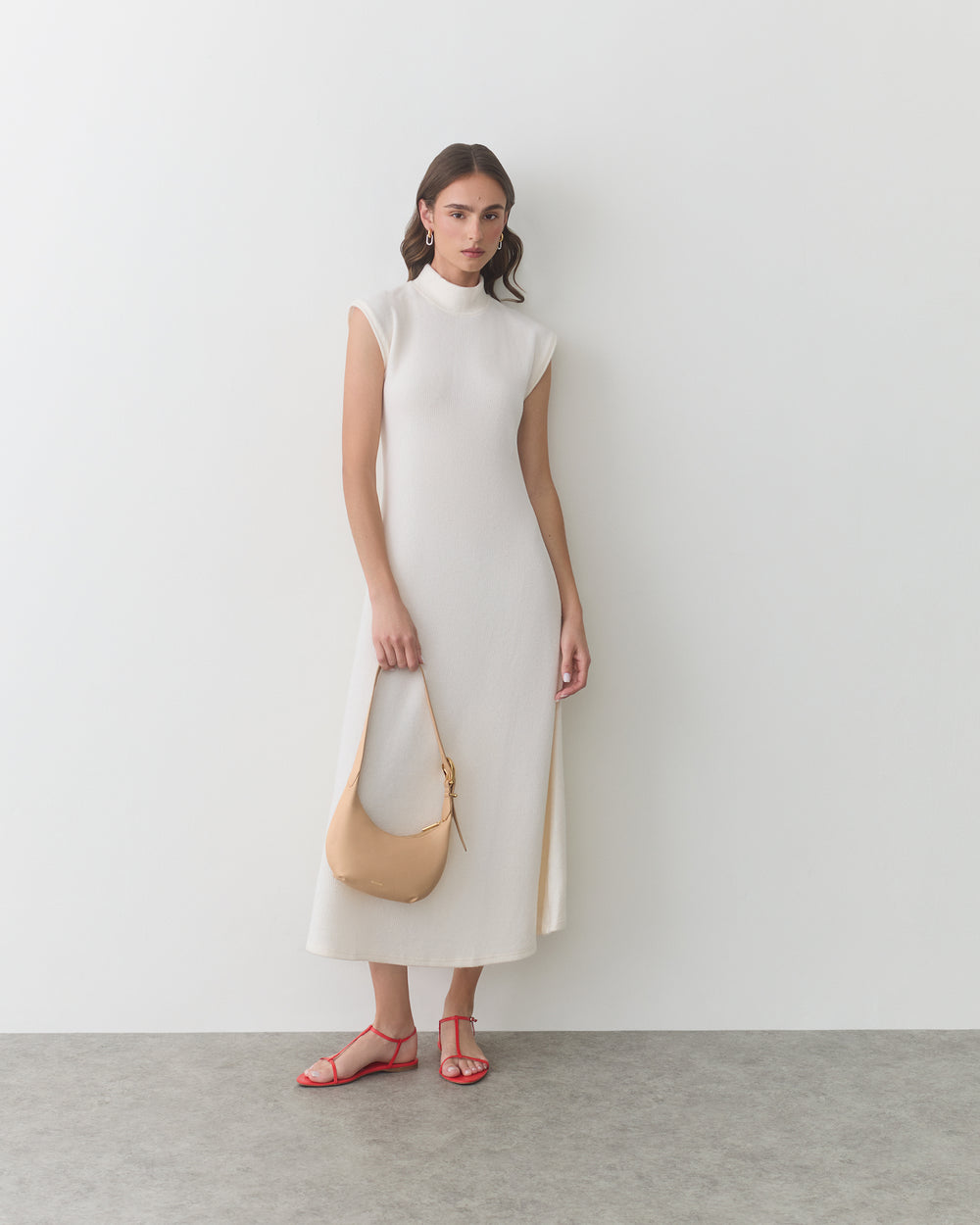 Woman in long sleeveless dress holding a handbag, wearing sandals.