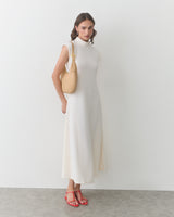 Woman standing in a sleeveless dress wearing a shoulder bag.