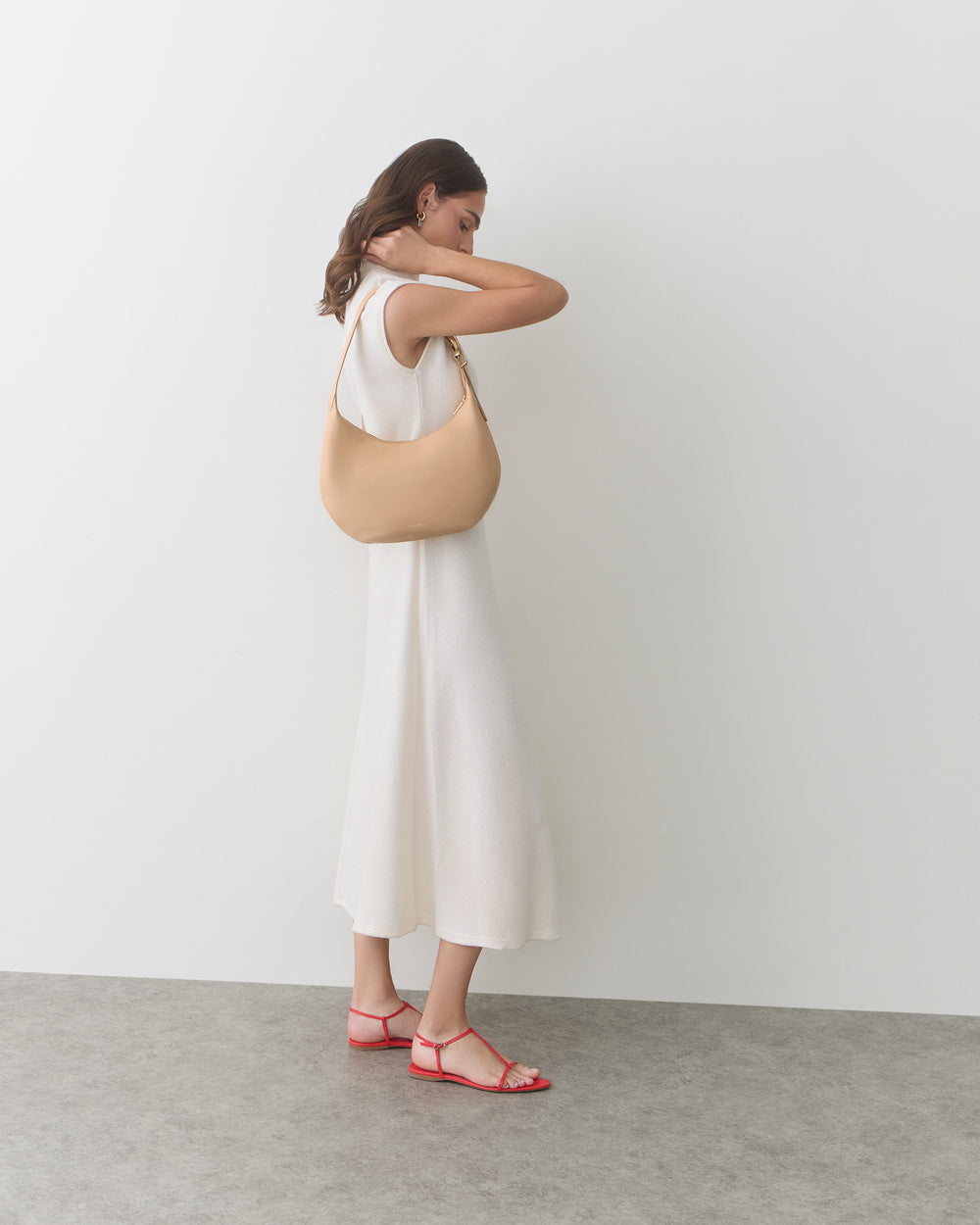 Person in a long dress holding a shoulder bag, standing against a plain backdrop.