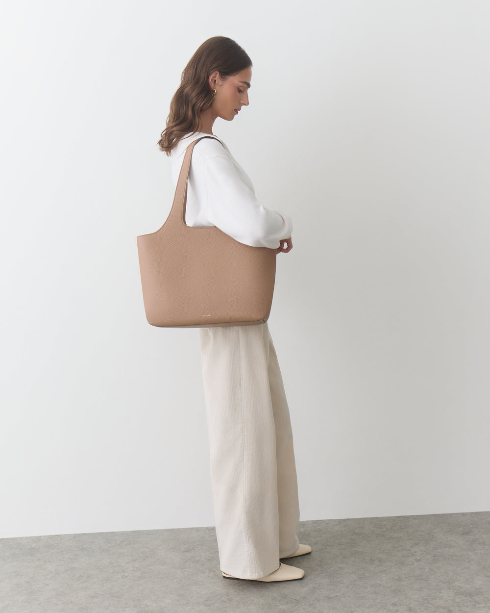 Person standing holding a tote bag and wearing wide-leg pants.