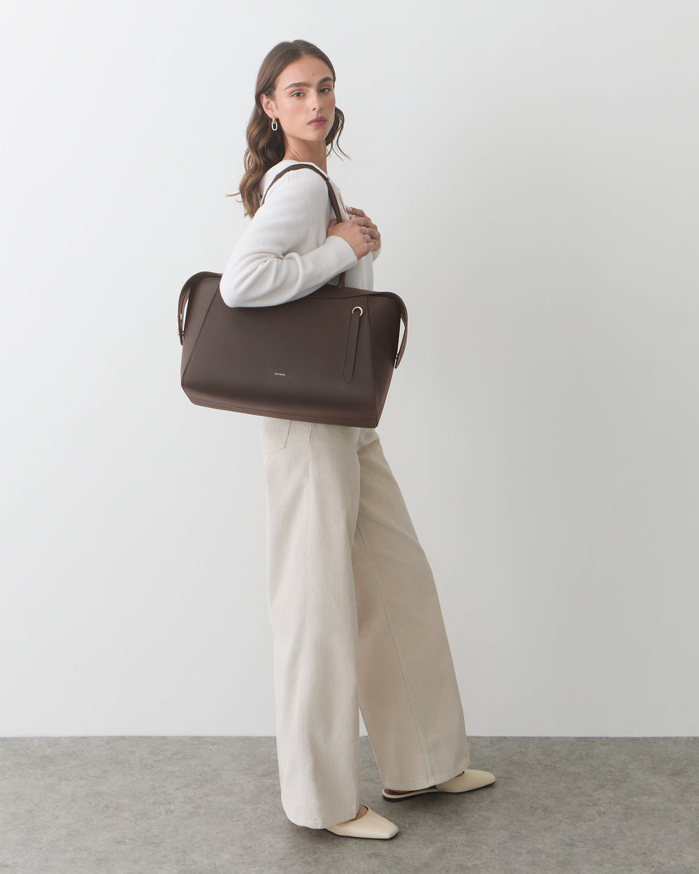 Person holding a travel bag, wearing a long-sleeve top and wide-leg pants.