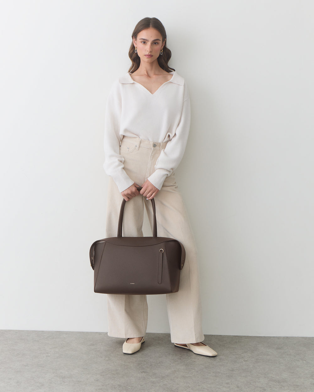 Person holding a travel bag, wearing a long-sleeve top and wide-leg pants.