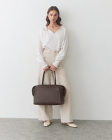 Person holding a travel bag, wearing a long-sleeve top and wide-leg pants.