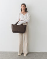 Person holding large handbag, wearing long sleeve top and wide-leg pants.