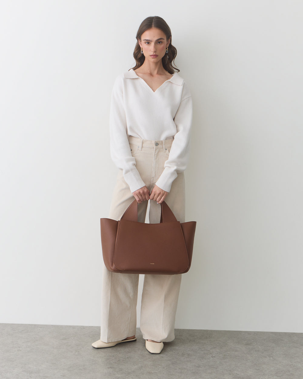 Person standing with a large tote bag in hand against a plain background.