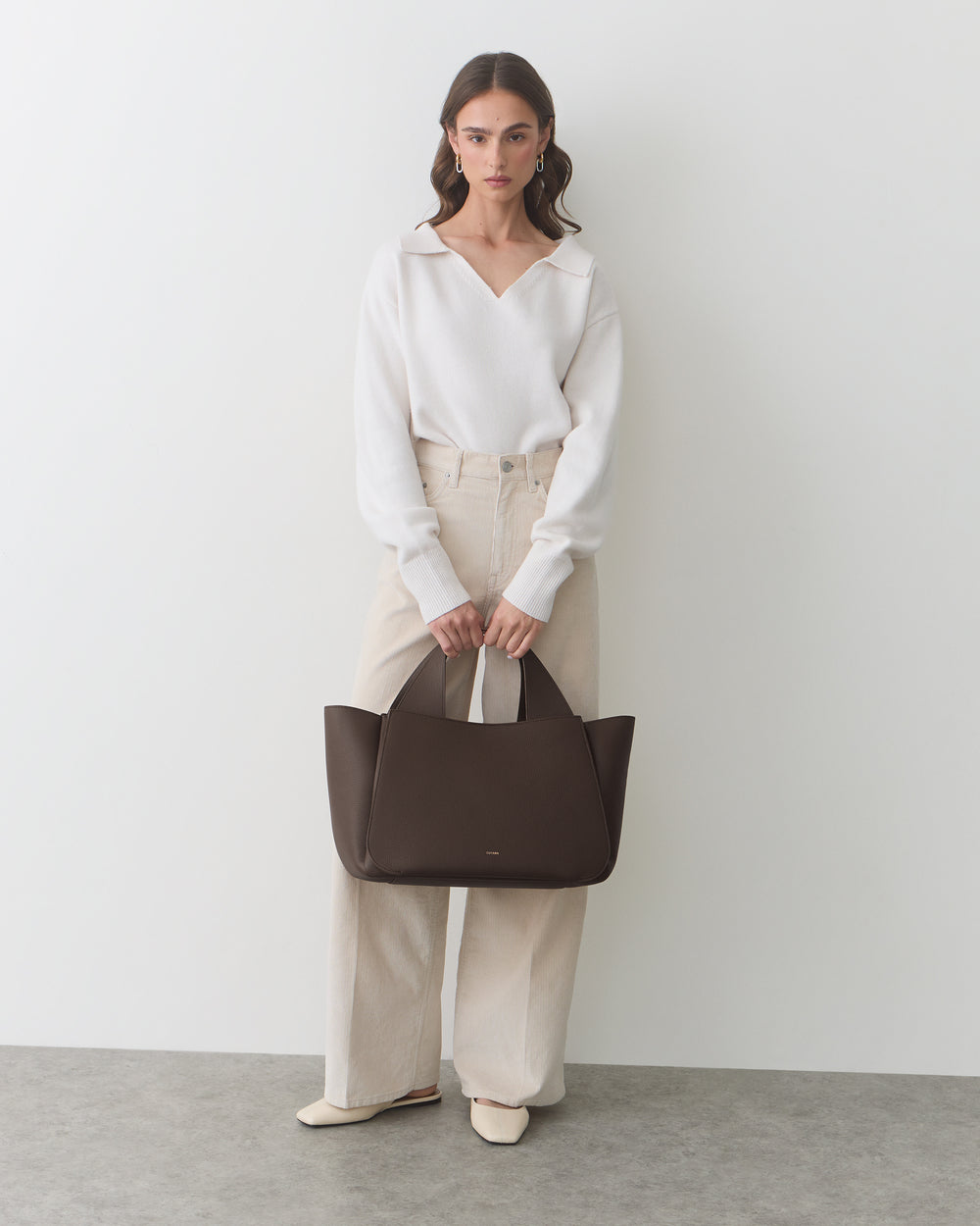 Person holding a large handbag wearing long-sleeve top and wide-leg pants.