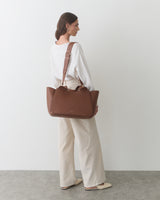 Person carrying a travel bag on shoulder, standing against a plain wall.