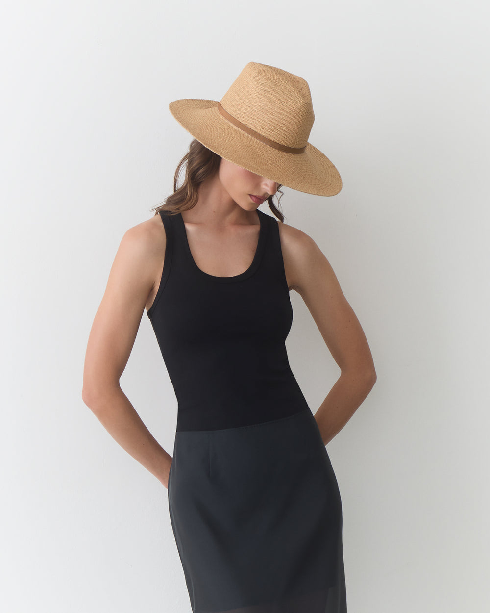 Person wearing a sleeveless top, skirt, and wide-brimmed hat, head tilted downward.