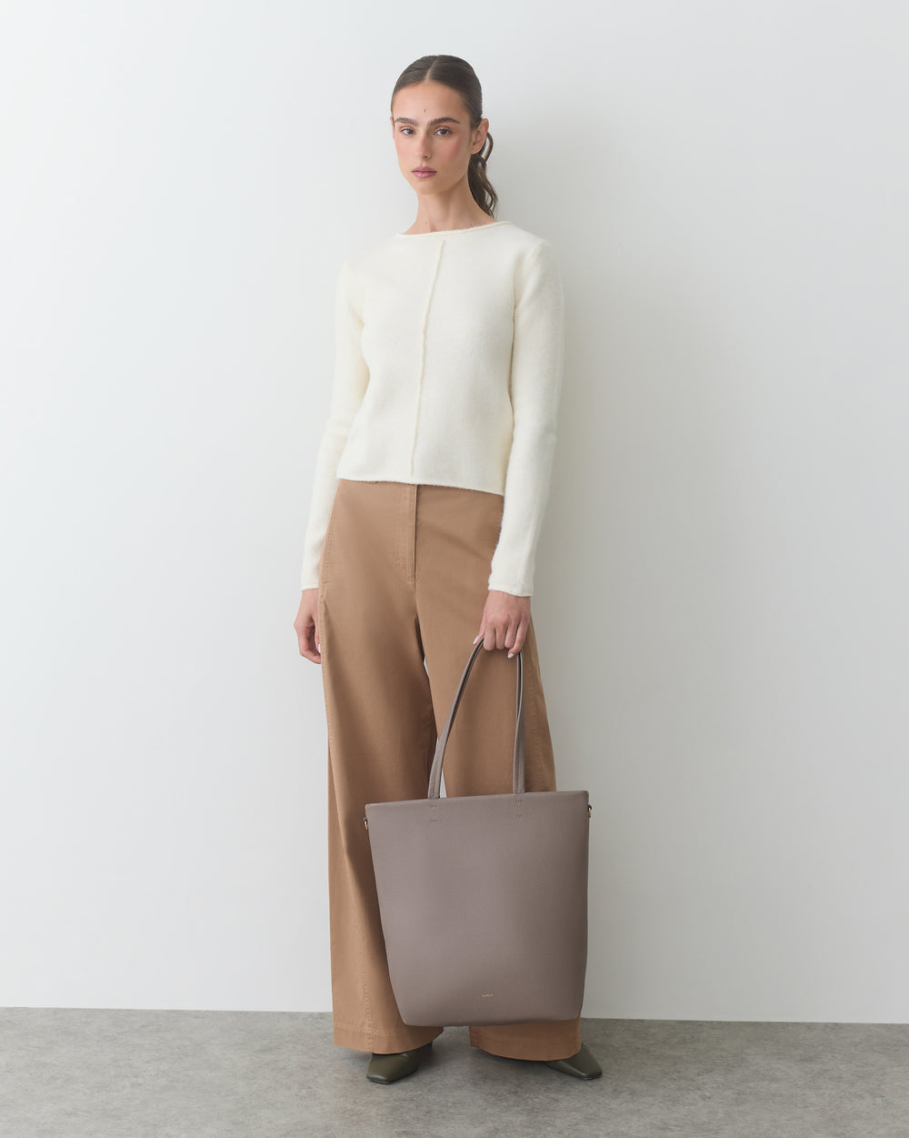Person holding a large handbag, wearing a long-sleeve shirt and wide-leg pants.