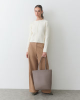 Person holding a large handbag, wearing a long-sleeve shirt and wide-leg pants.