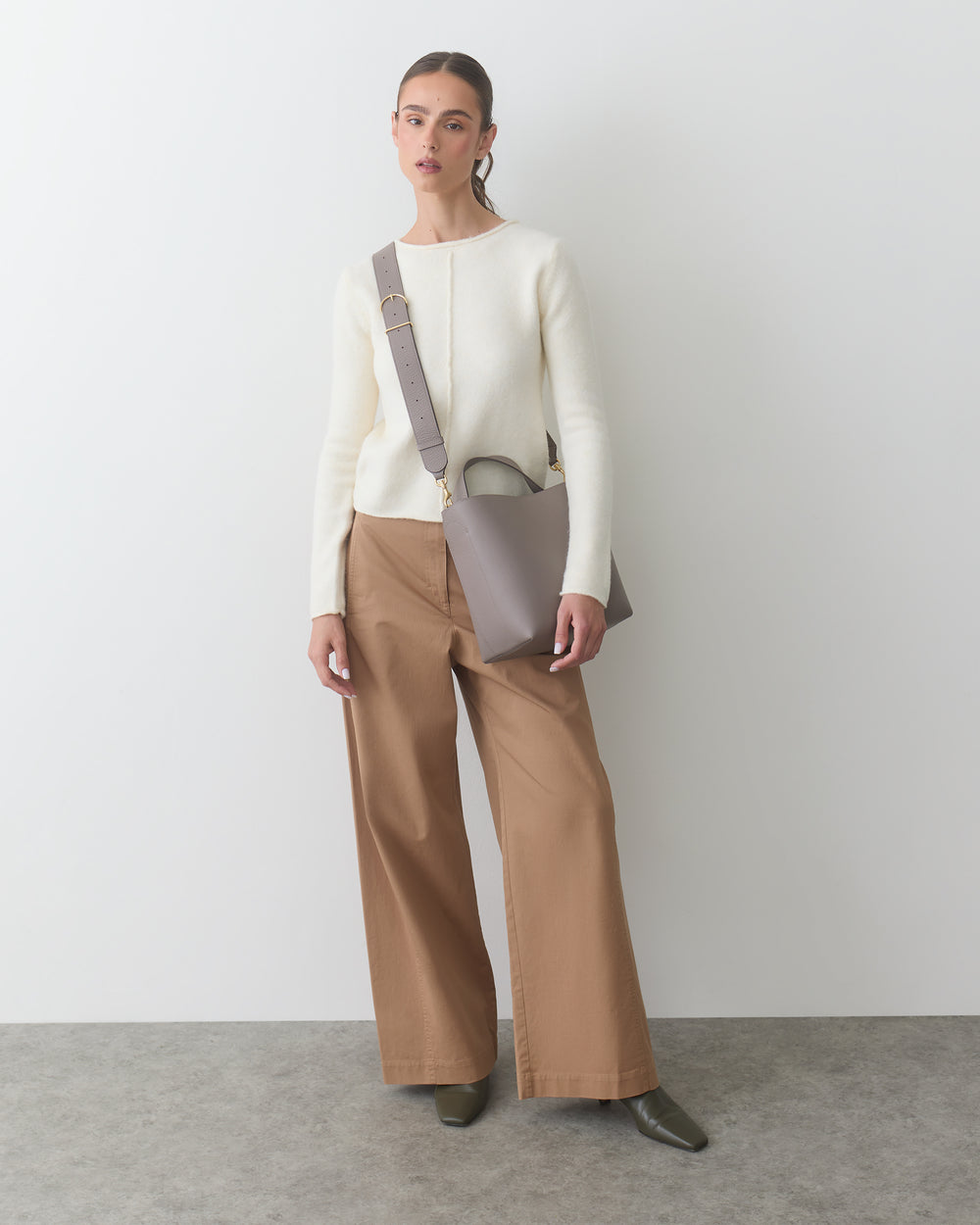 Person wearing a sweater and wide-leg pants, holding a shoulder bag.