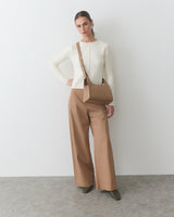Person in long-sleeve top and wide-leg pants, holding a shoulder bag.