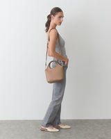 Person standing with handbag over shoulder, wearing a sleeveless top and jeans.