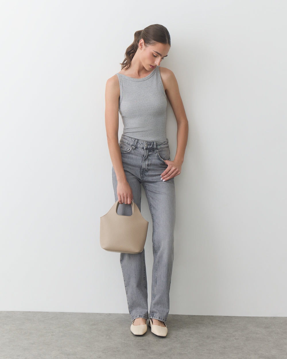 Person in tank top and jeans holding a handbag, looking down.