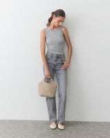 Person in tank top and jeans holding a handbag, looking down.