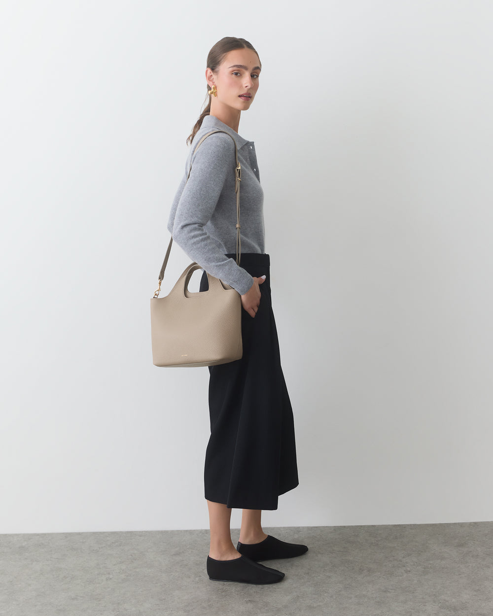 Person standing with shoulder bag, wearing a sweater and long skirt.