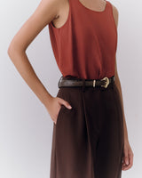 Person wearing a sleeveless top and belted pants with a hand in pocket.