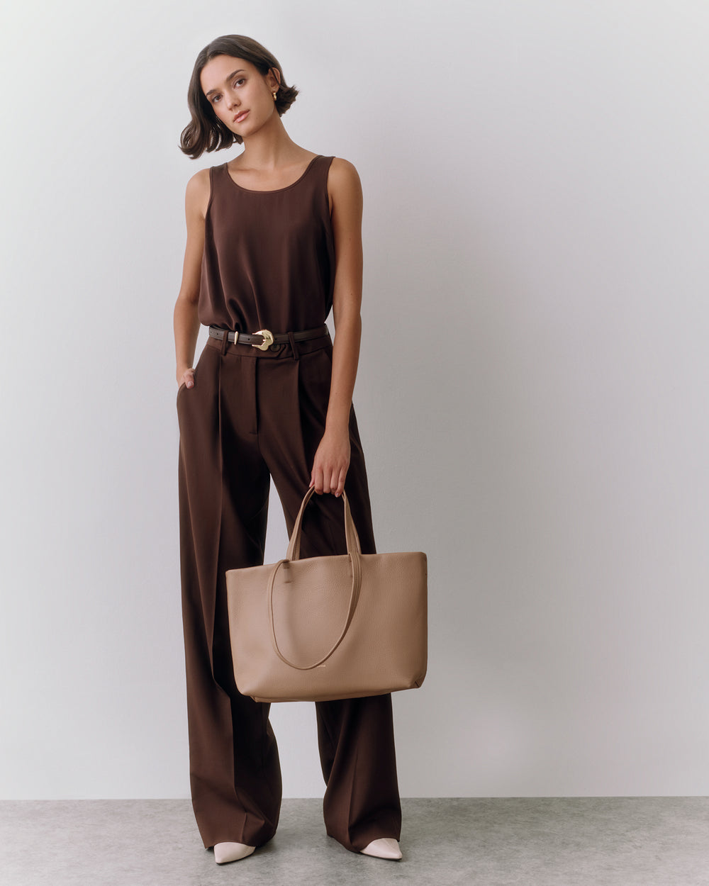 Person in sleeveless top and trousers holding a large tote bag.