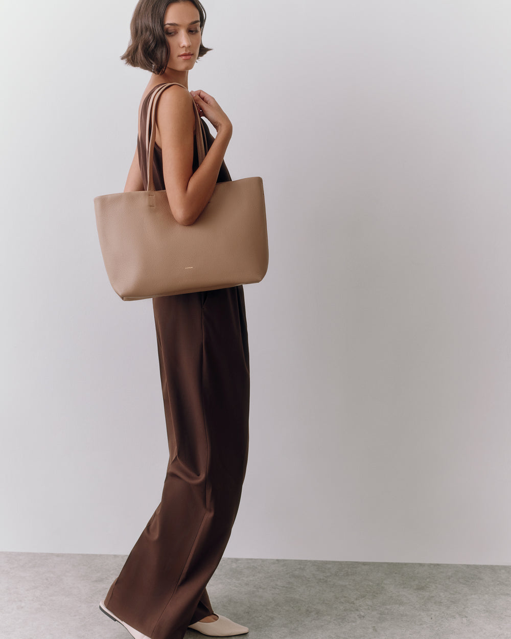 Person in a dress holding a large tote bag standing sideways.