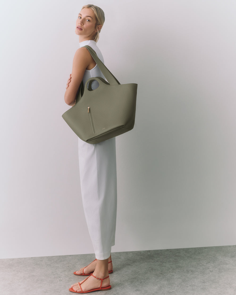 Person standing with large tote bag and wearing sandals against a plain background.