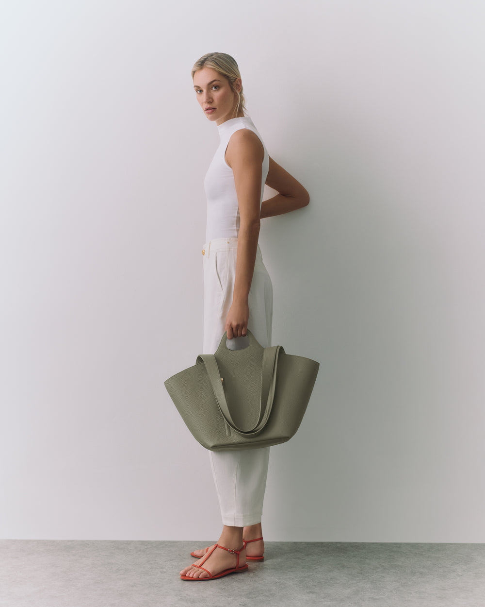 Person in a sleeveless top holding a large tote bag, wearing sandals.