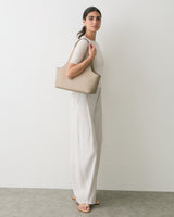 Person standing with a handbag over shoulder, wearing a top and wide-leg pants