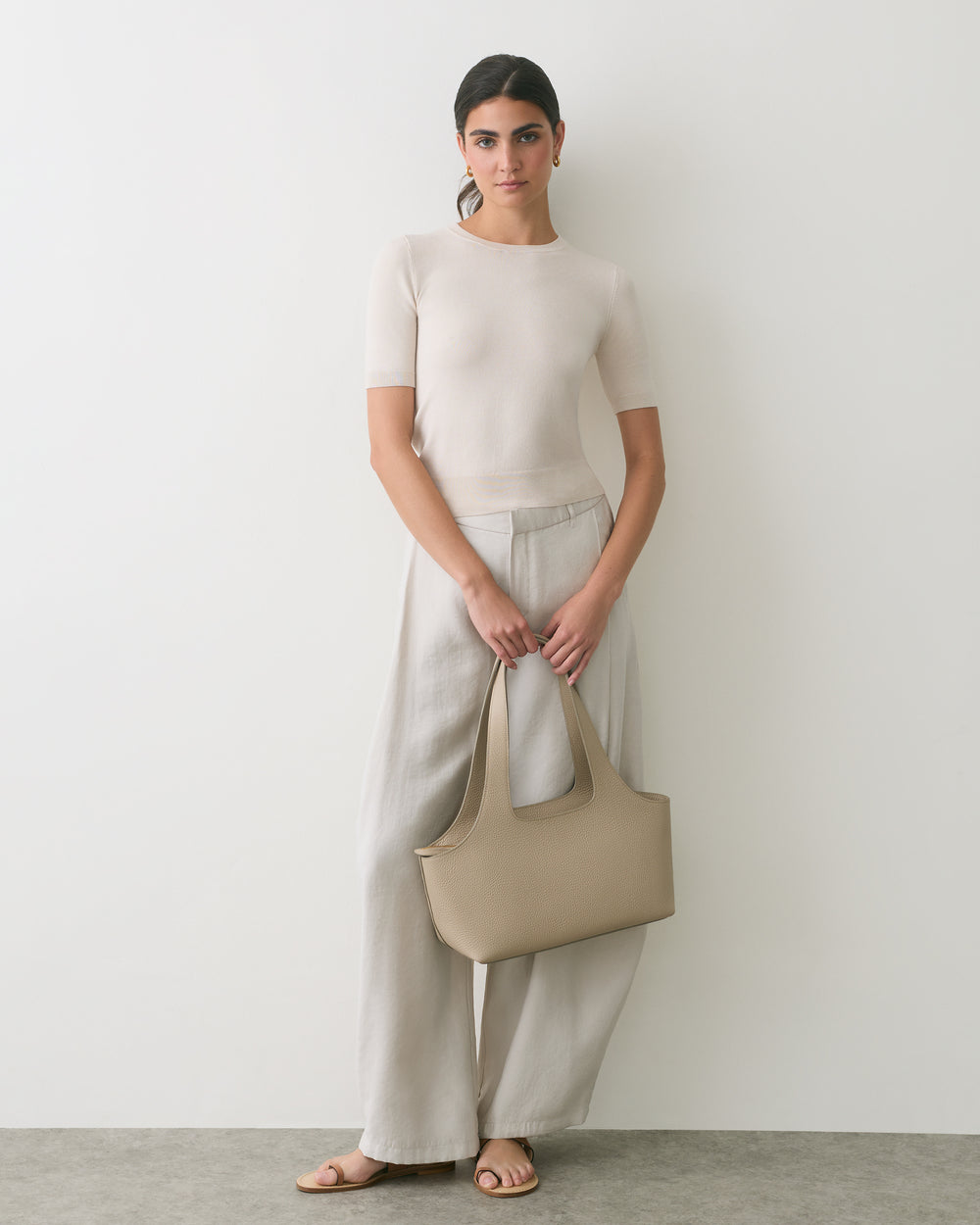 Person standing, holding a handbag, wearing a shirt and wide-leg pants.