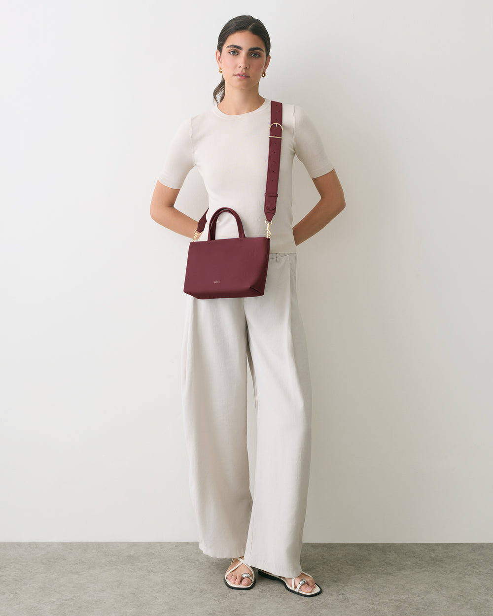 Person standing with crossbody bag and relaxed-fit pants.