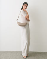 Person in a simple outfit holding a shoulder bag, standing sideways.