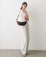 Person standing with a shoulder bag and wearing sandals.