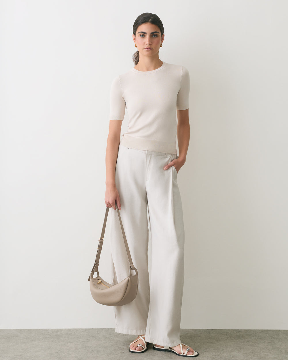 Person wearing short-sleeve top and wide-leg pants holds a shoulder bag and wears sandals.