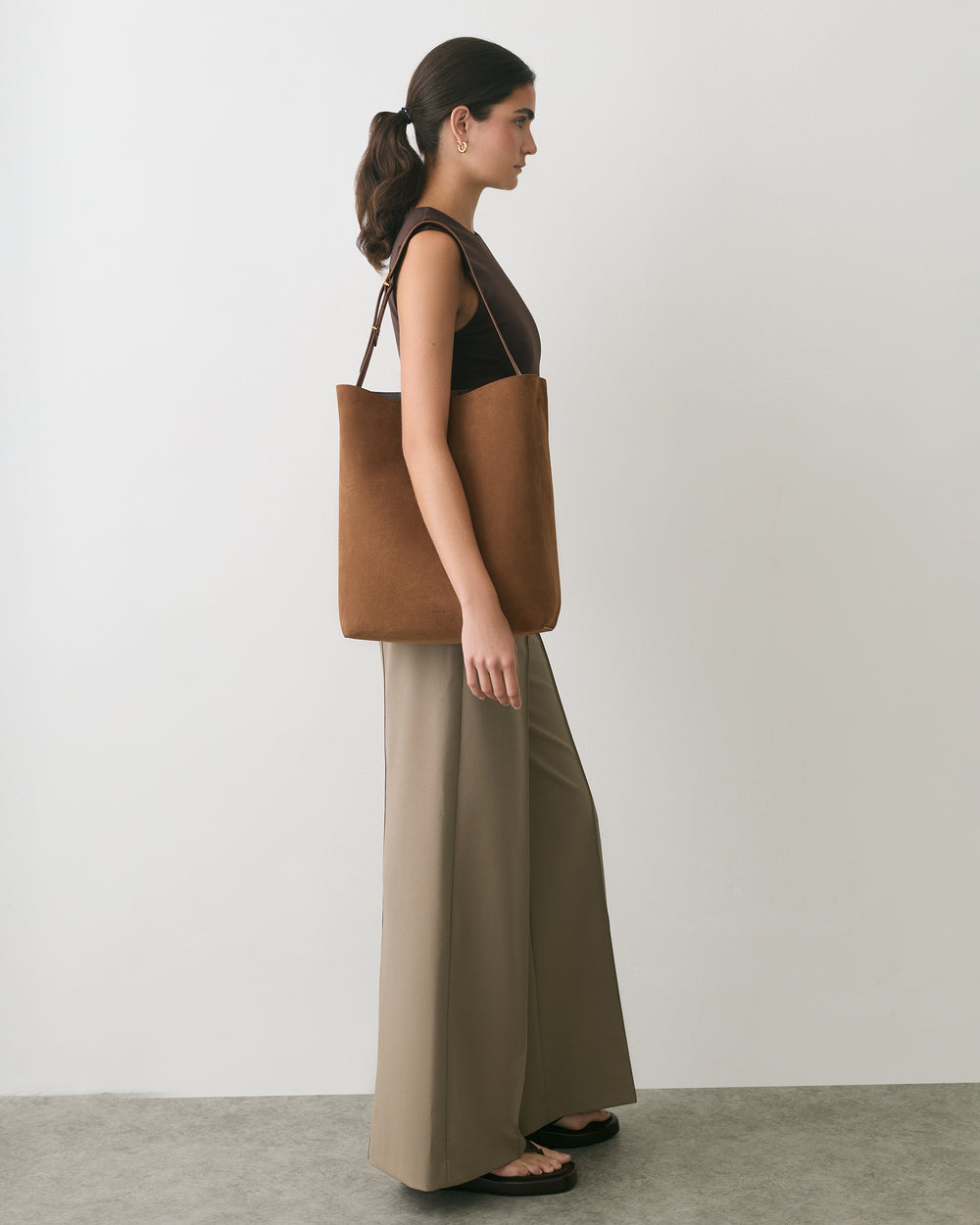 Person standing sideways with a tote bag wearing a sleeveless top and wide-leg pants.