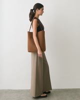 Person standing sideways with a tote bag wearing a sleeveless top and wide-leg pants.