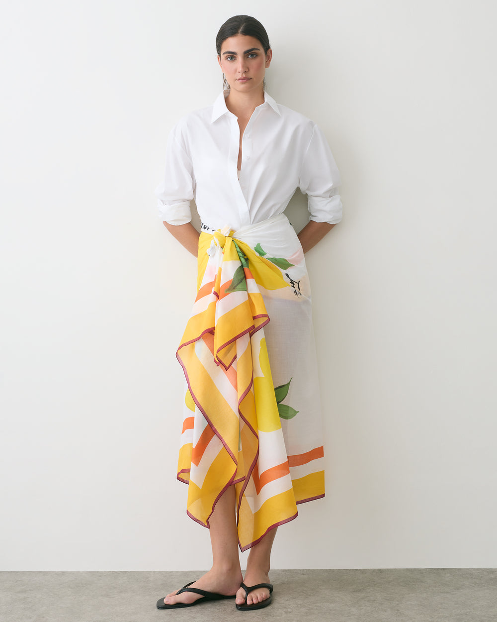 Person wearing a white shirt, floral patterned skirt, and sandals standing indoors.