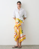 Person wearing a white shirt, floral patterned skirt, and sandals standing indoors.