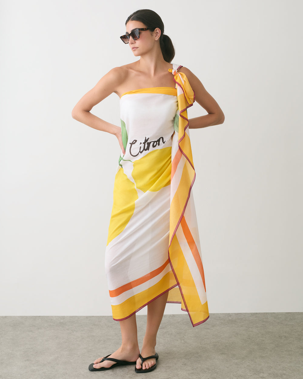 Person wearing a patterned one-shoulder dress with sunglasses and sandals.