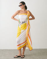 Person wearing a patterned one-shoulder dress with sunglasses and sandals.