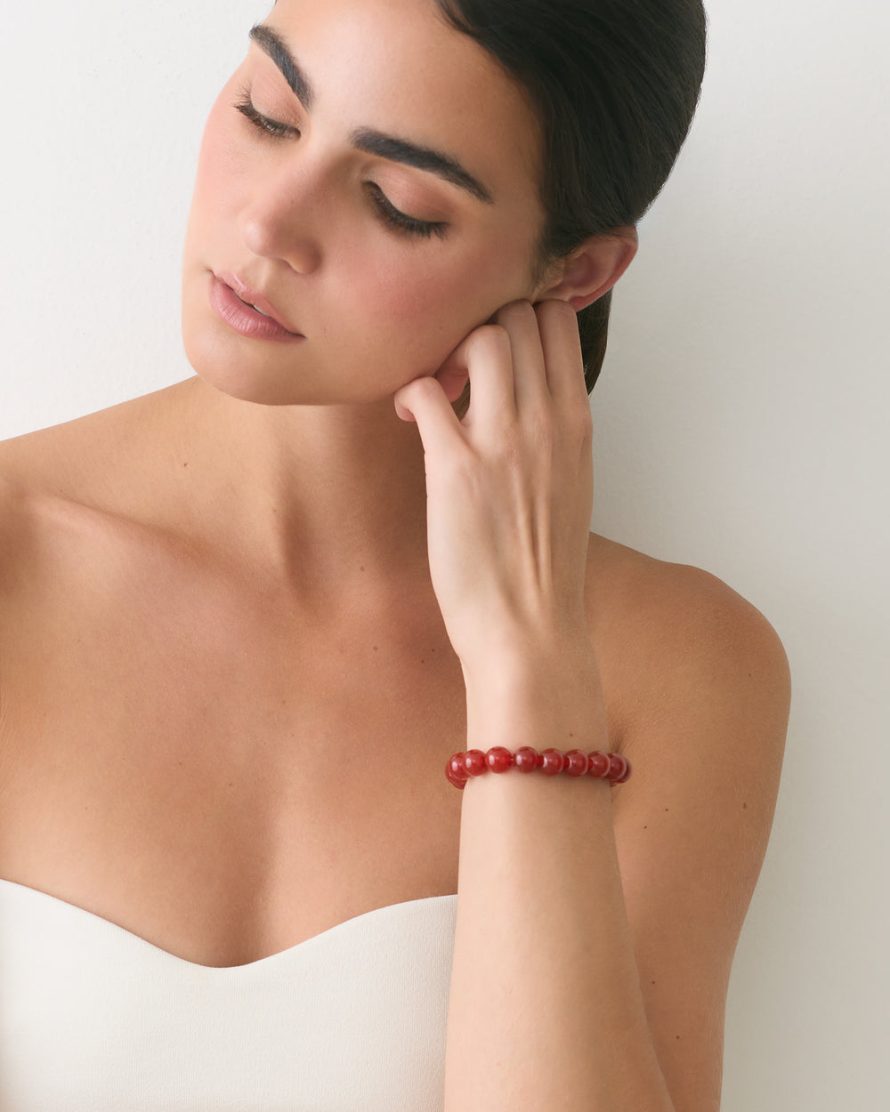 Person wearing a strapless top and bracelet, looking down.