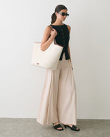 Person wearing sleeveless top and wide-leg pants, holding a large tote bag, wearing sunglasses.