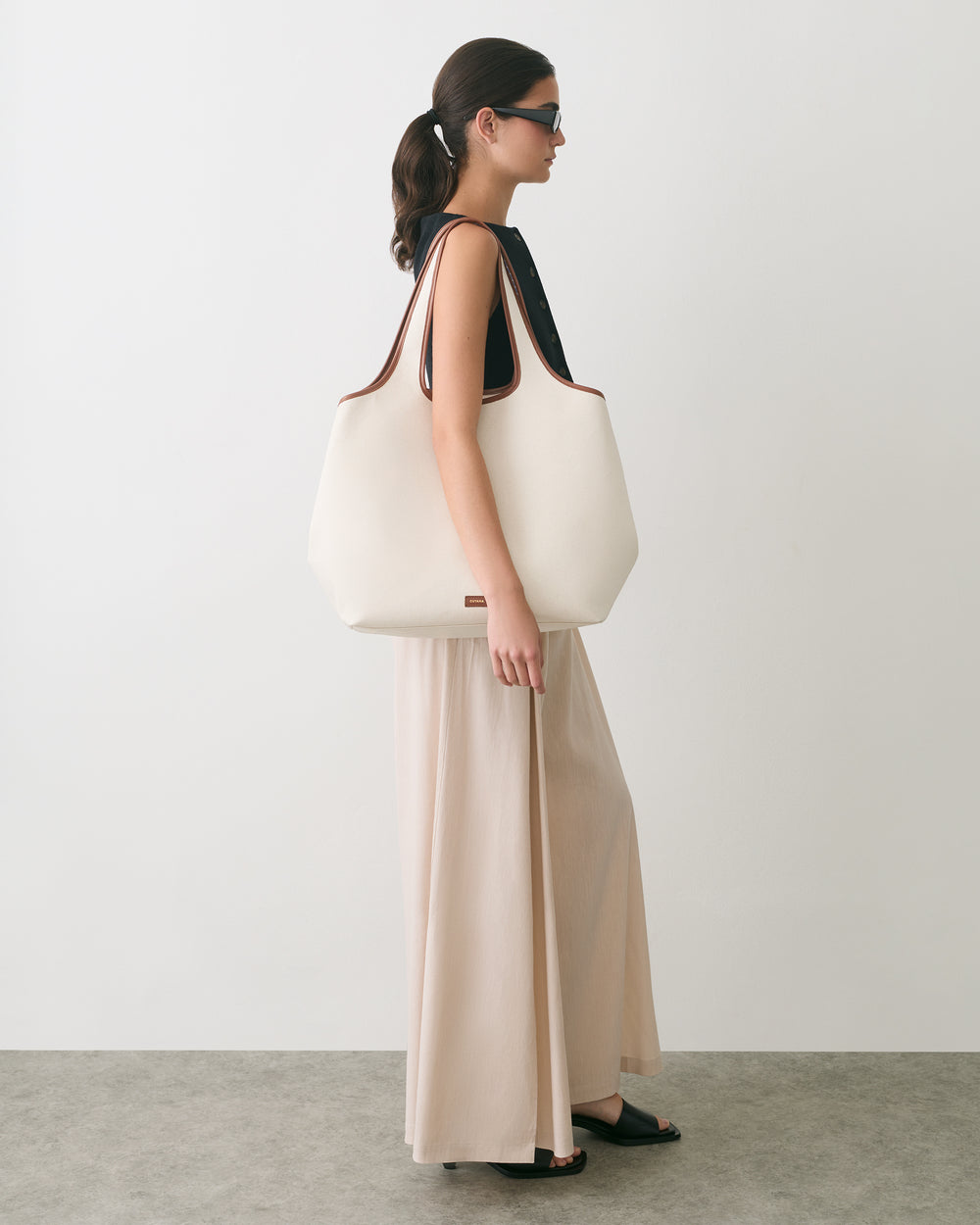 Person wearing a sleeveless top and long skirt holding a large shoulder bag.