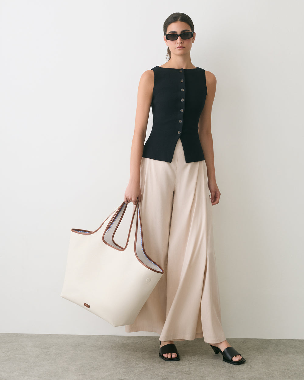 Person wearing sleeveless top and wide pants, holding large bag, and wearing sunglasses.
