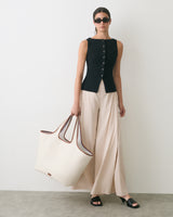 Person wearing sleeveless top and wide pants, holding large bag, and wearing sunglasses.