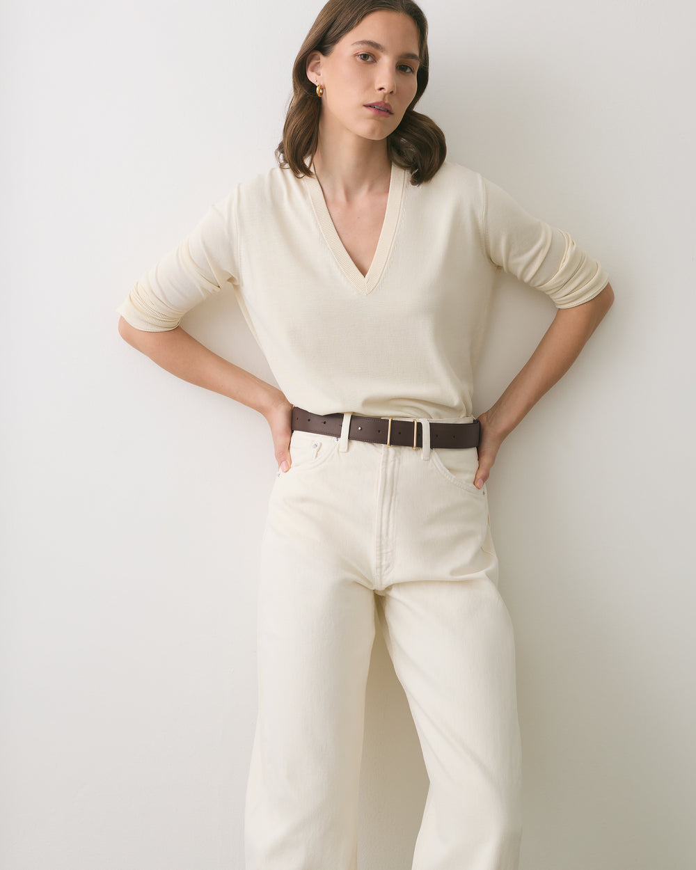 Person wearing a long-sleeve shirt and pants with a belt, standing against a wall.