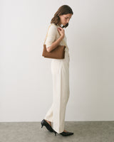 Person standing sideways with a handbag wearing a top and wide-leg pants.